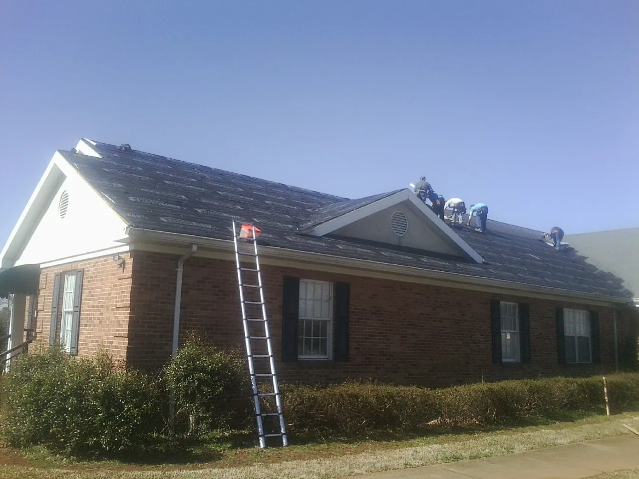 Crew tearing shingles off a brick ranch roof with a ladder set — Emergency Roof Repair work by our crew in Equinunk