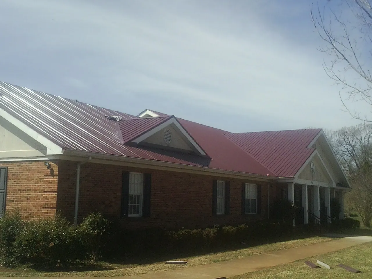 Red metal roof with gabled entries on a long brick building, from a Hail Damage Roof Repair job in Equinunk