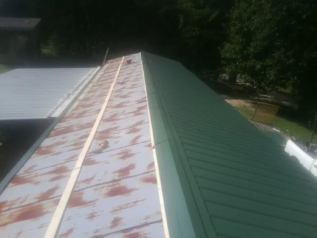 Old rusted panels beside newly installed green metal roofing — Wind Damage Roof Repair by Roofing Brothers in Equinunk
