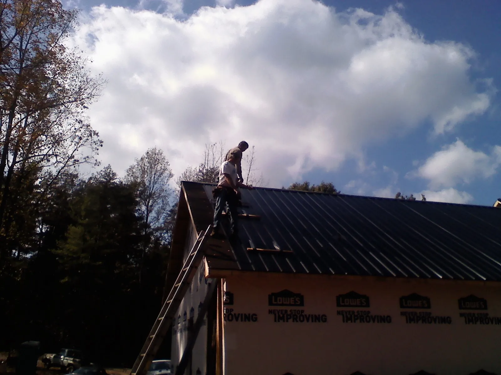 Roofer fastening dark metal panels high against a cloudy sky, from a Roof Inspection job in Equinunk